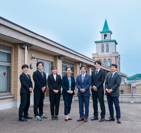 百瀬理事長（右から3人目）と教員。フェリシア高等学校の鐘楼を臨む屋上スカイガーデンにて